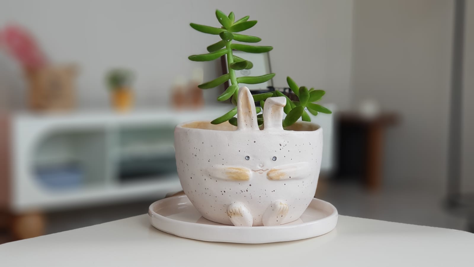 Handcrafted ceramic planter with bunny ears cradling a green succulent.