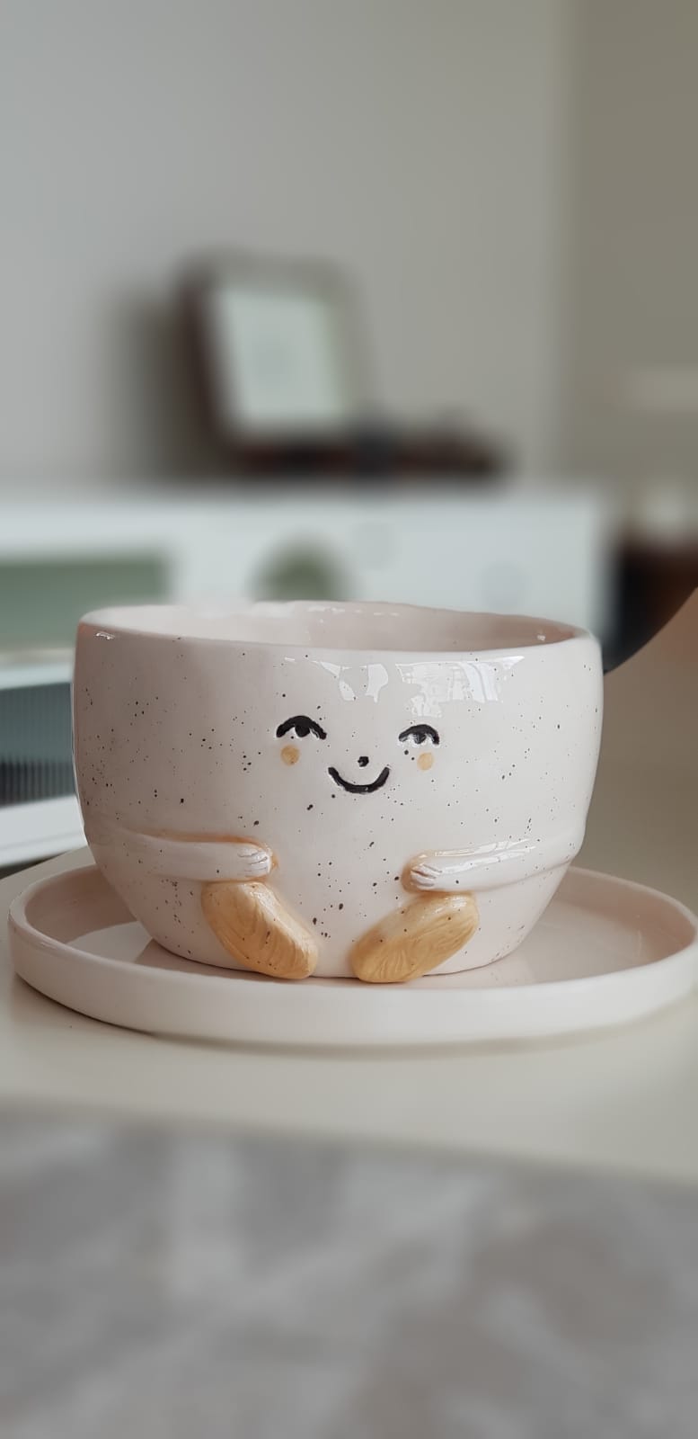 Smiling ceramic planter with arms gently resting on a matching saucer.